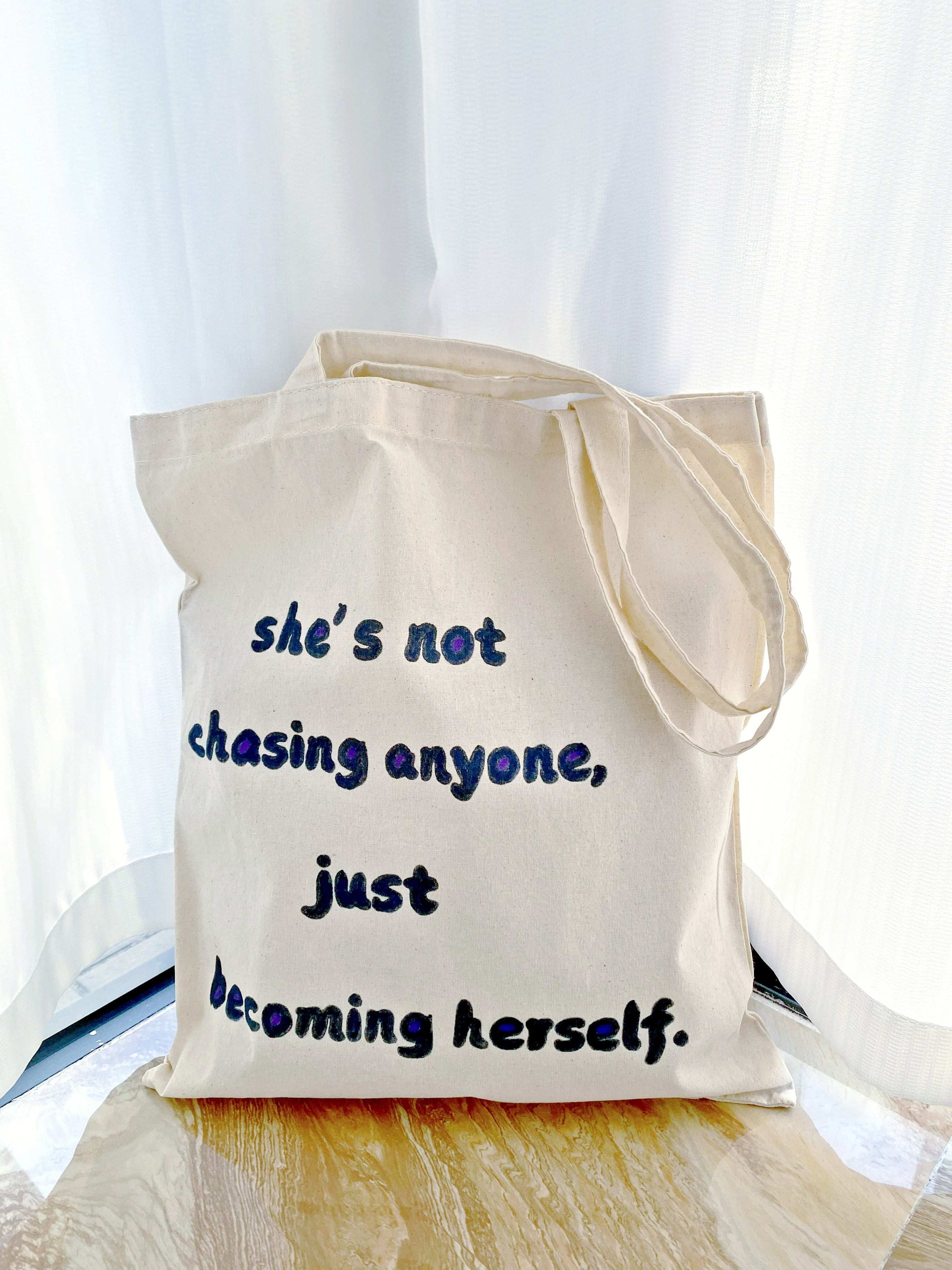 A sustainable cotton tote bag with an inspirational quote hand-painted on the front, perfect for running errands or casual outings.